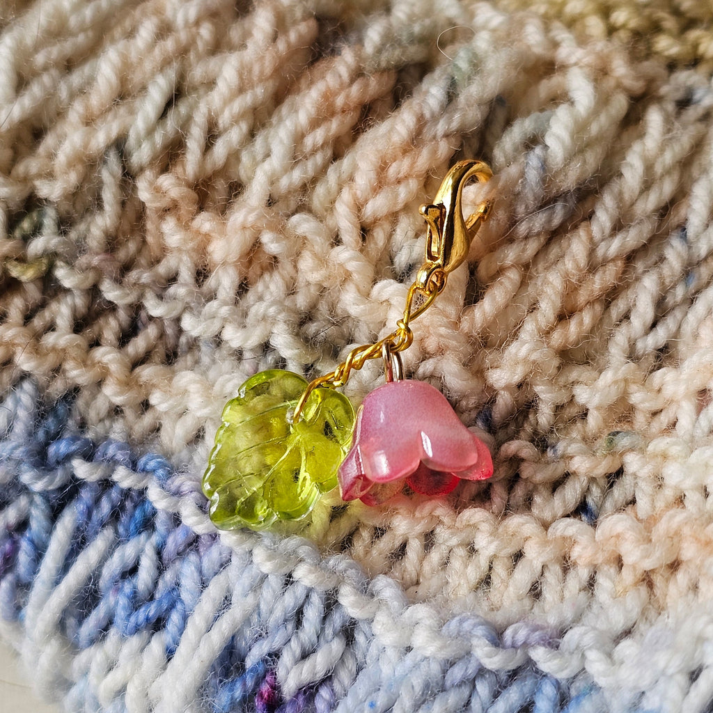 Small charm with green leaf and pink flower on a textured fabric background